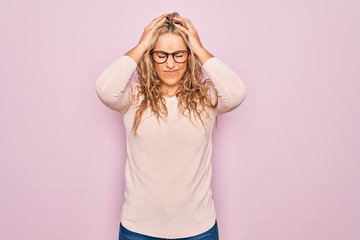 Young beautiful blonde woman wearing casual sweater and glasses over pink background suffering from headache desperate and stressed because pain and migraine. Hands on head.