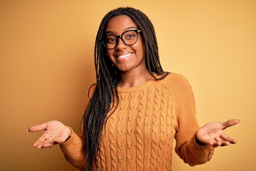 Young african american smart woman wearing glasses and casual sweater over yellow background...