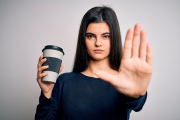 Young beautiful brunette woman drinking cup of coffee over isolated white background with open hand doing stop sign with serious and confident expression, defense gesture