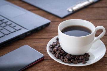 
Black coffee in a white coffee mug on top and a notebook on a wooden table, wooden table
