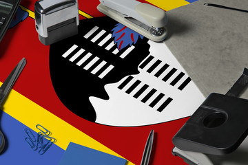 Swaziland flag with office clerk workplace background. National stationary concept with office tools.