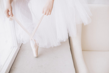 Ballet dancer's feet on studio floor. Teenage dancer puts on ballet pointe shoes. Elegance and...