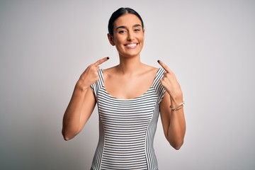 Young beautiful brunette woman wearing casual striped dress over isolated white background smiling cheerful showing and pointing with fingers teeth and mouth. Dental health concept.