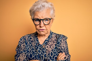 Senior beautiful grey-haired woman wearing casual shirt and glasses over yellow background skeptic...