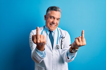 Middle age handsome grey-haired doctor man wearing coat and blue stethoscope Showing middle finger...