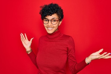 Young beautiful african american afro woman wearing turtleneck sweater and glasses clueless and confused expression with arms and hands raised. Doubt concept.