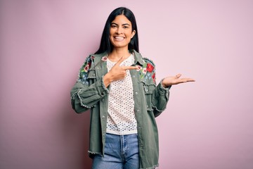 Young beautiful hispanic fashion woman wearing cool jacket over pink background amazed and smiling to the camera while presenting with hand and pointing with finger.