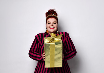 Overweight ginger female in striped dress, crown and earrings. Holding golden gift box, excited,...