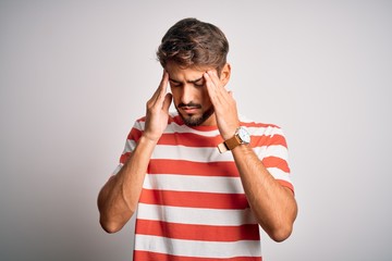 Young handsome man with beard wearing striped t-shirt standing over white background with hand on head for pain in head because stress. Suffering migraine.