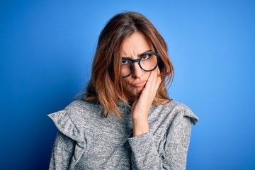 Young beautiful brunette woman wearing casual sweater and glasses over blue background thinking looking tired and bored with depression problems with crossed arms.