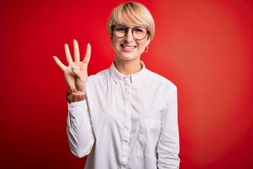 Young blonde business woman with short hair wearing glasses over red background showing and pointing up with fingers number four while smiling confident and happy.