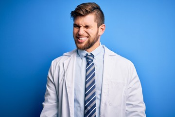 Young blond therapist man with beard and blue eyes wearing coat and tie over background winking looking at the camera with sexy expression, cheerful and happy face.