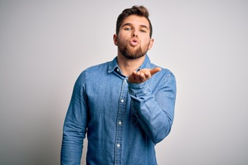 Young handsome blond man with beard and blue eyes wearing casual denim shirt looking at the camera blowing a kiss with hand on air being lovely and sexy. Love expression.