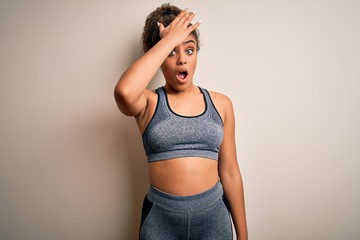 Young african american sportswoman doing sport wearing sportswear over white background surprised...