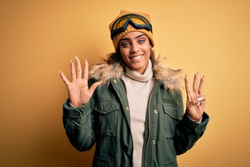 Young african american afro skier girl wearing snow sportswear and ski goggles showing and pointing up with fingers number eight while smiling confident and happy.