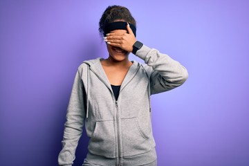 Obraz premium Young african american sportswoman doing sport wearing sportswear over purple background smiling and laughing with hand on face covering eyes for surprise. Blind concept.
