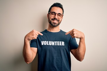 Fototapeta premium Handsome man with beard wearing t-shirt with volunteer message over white background looking confident with smile on face, pointing oneself with fingers proud and happy.