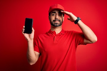 Young handsome delivery man with beard holding smartphone showing deliver food app stressed with hand on head, shocked with shame and surprise face, angry and frustrated. Fear and upset for mistake.