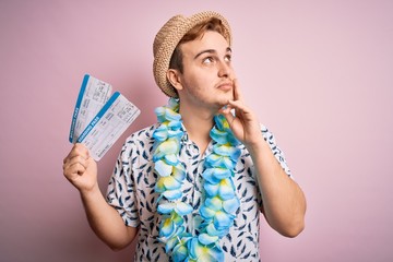 Handsome redhead tourist man on vacation wearing hawaiian lei holding boarding pass airlane serious...
