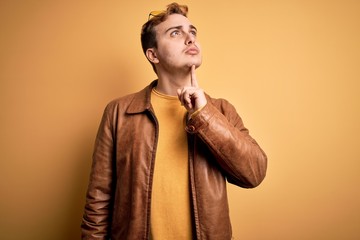 Fototapeta premium Young handsome redhead man wearing casual leather jacket over isolated yellow background Thinking concentrated about doubt with finger on chin and looking up wondering