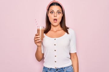 Young beautiful brunette woman drinking glass of chocolate beverage using straw scared and amazed...