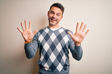 Young handsome man wearing casual sweater standing over isolated white background showing and pointing up with fingers number ten while smiling confident and happy.