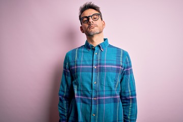 Young handsome man wearing casual shirt and glasses standing over isolated pink background Relaxed with serious expression on face. Simple and natural looking at the camera.