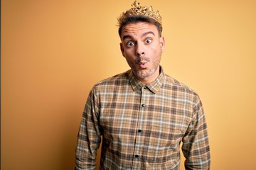 Young handsome man wearing golden crown of king over isolated yellow background afraid and shocked with surprise expression, fear and excited face.