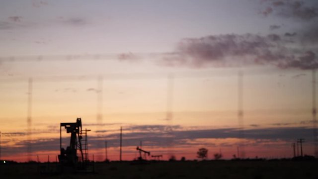 Silhouettes of oil drills activated in a field at sunset in rural Texas