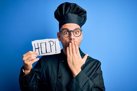 Young handsome chef man overworked wearing uniform and hat holding help paper message cover mouth with hand shocked with shame for mistake, expression of fear, scared in silence, secret concept