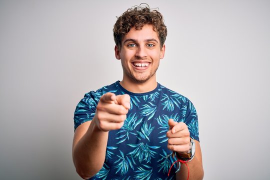 Young blond handsome man on vacation with curly hair wearing casual summer t-shirt pointing fingers to camera with happy and funny face. Good energy and vibes.
