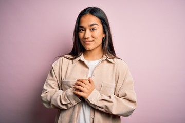 Young beautiful asian woman wearing casual shirt standing over pink background with hands together and crossed fingers smiling relaxed and cheerful. Success and optimistic