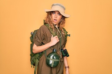 Young blonde explorer woman with blue eyes hiking wearing backpack and water canteen In shock face, looking skeptical and sarcastic, surprised with open mouth