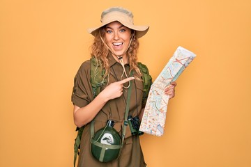 Young blonde explorer woman with blue eyes hiking wearing backpack holding city map very happy...