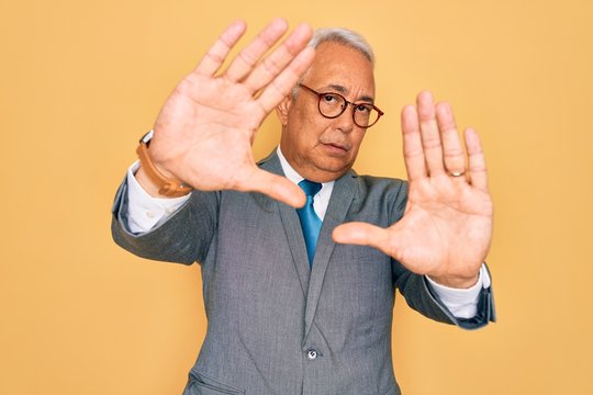 Middle age senior grey-haired handsome business man wearing glasses over yellow background doing frame using hands palms and fingers, camera perspective