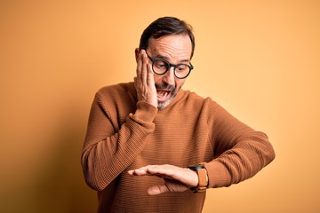 Middle age hoary man wearing brown sweater and glasses over isolated yellow background Looking at...