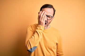 Middle age hoary man wearing casual sweater and glasses over isolated yellow background Yawning tired covering half face, eye and mouth with hand. Face hurts in pain.