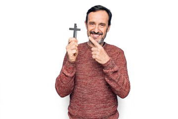 Middle age handsome catholic man praying holding christian cross over isolated background smiling...