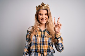 Young beautiful blonde woman wearing golden crown of queen over isolated white background smiling...