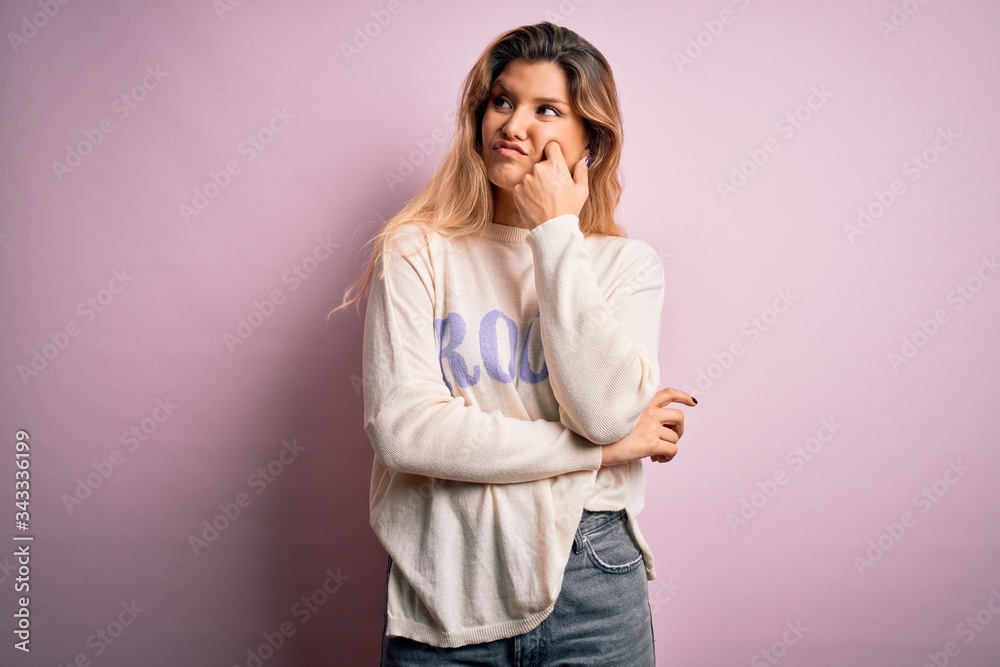 Poster Young beautiful blonde woman wearing casual sweater standing over pink background with hand on chin thinking about question, pensive expression. Smiling with thoughtful face. Doubt concept.