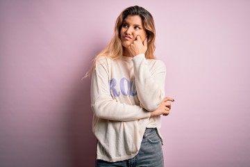 Young beautiful blonde woman wearing casual sweater standing over pink background with hand on chin thinking about question, pensive expression. Smiling with thoughtful face. Doubt concept.