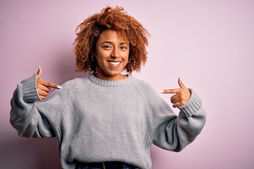 Young beautiful African American afro woman with curly hair wearing casual sweater looking...