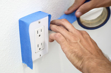 Painter Man Using Masking Blue Tape to Secure Electric Outlet.