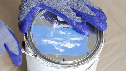Gloved hand opening a can of white paint with can opener before starting paint