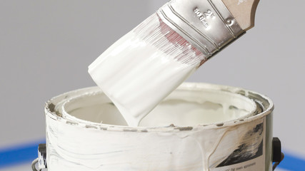 Hand of painter dipping a brush into a bucket with white paint. Renovation