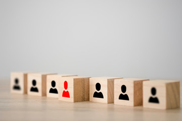 Red human icon on a wooden cube in front of other black human icon wooden cubes. Leadership and...