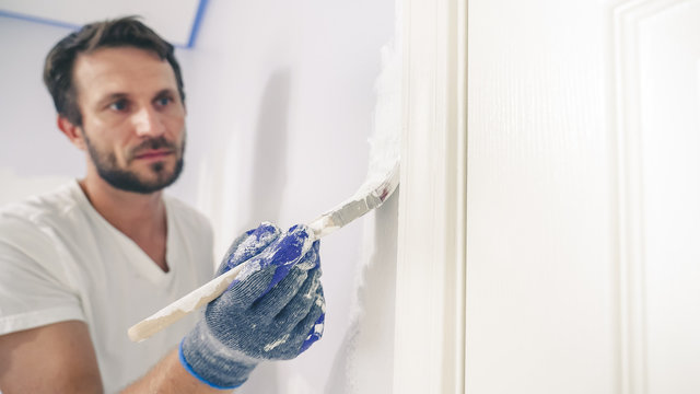 Close up of painter hands with gloves painting the wall edge by door frame.