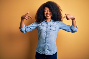 Young beautiful african american woman with afro hair standing over yellow isolated background...