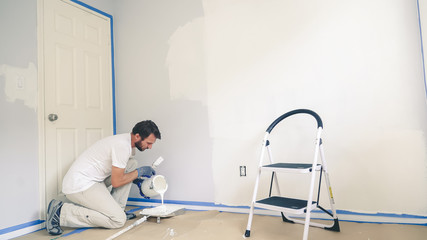 Professional interior construction worker pouring white color paint to tray.