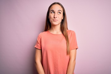 Fototapeta premium Young beautiful woman wearing casual t-shirt standing over isolated pink background smiling looking to the side and staring away thinking.